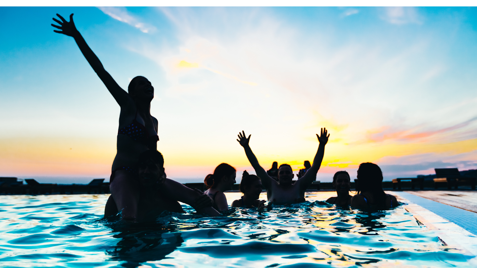 A group of women and men enjoying party in an infinity pool during the sunset
